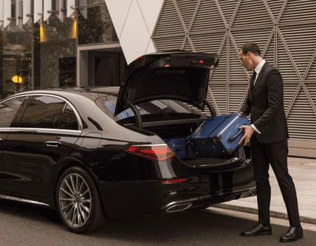 A professional chauffeur putting luggage of the passenger in the luxury black Mercedes sedan