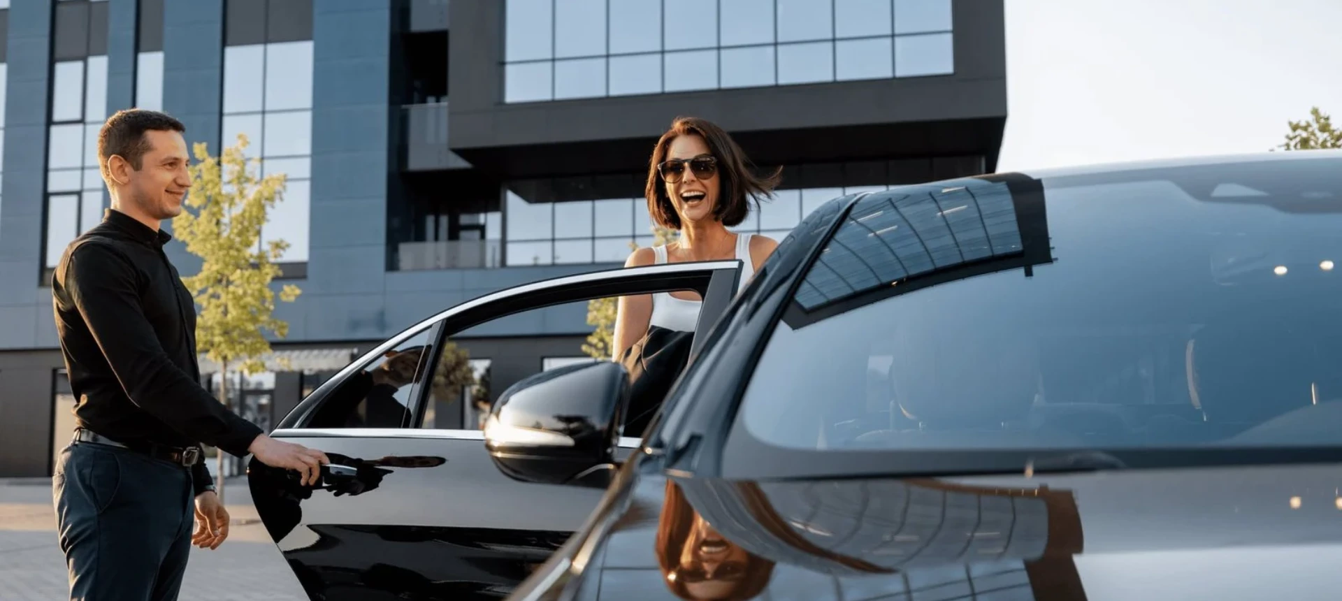 A professional chauffeur opening door of a luxury black sedan for a female passenger