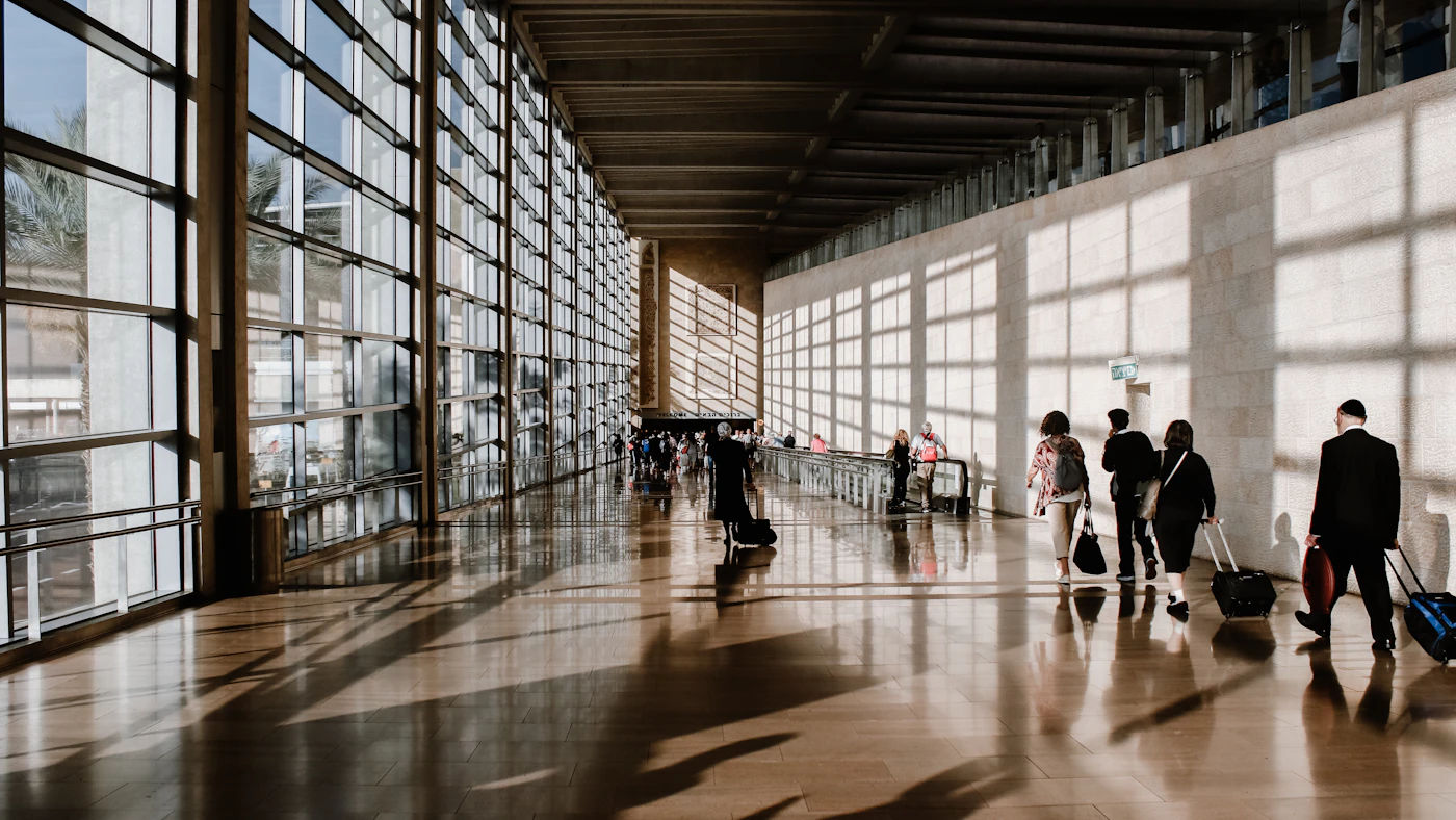Travelers walking through an airport corridor with rolling luggage